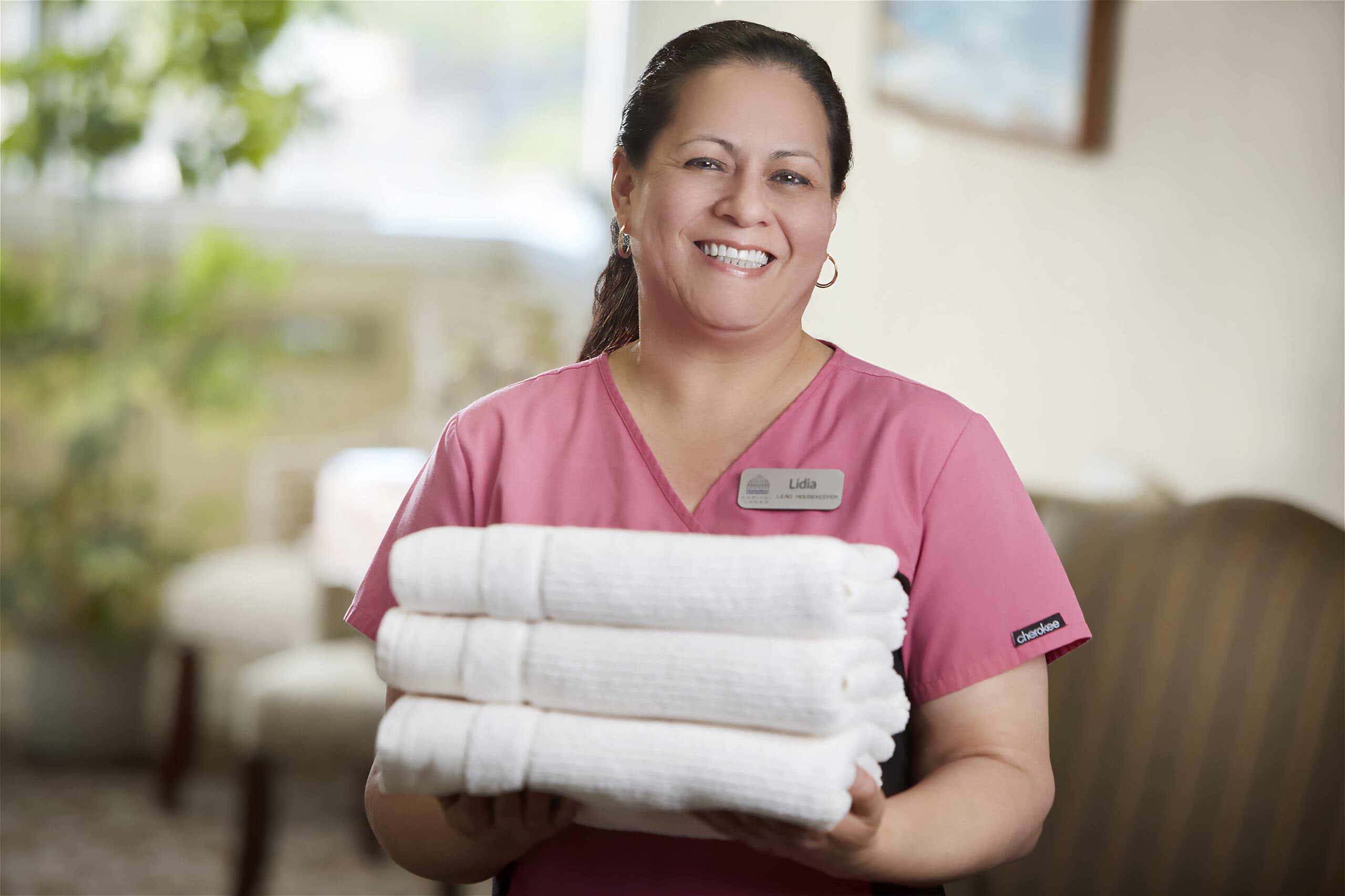 A smiling Capitol Lakes healthcare worker holds a stack of towels.